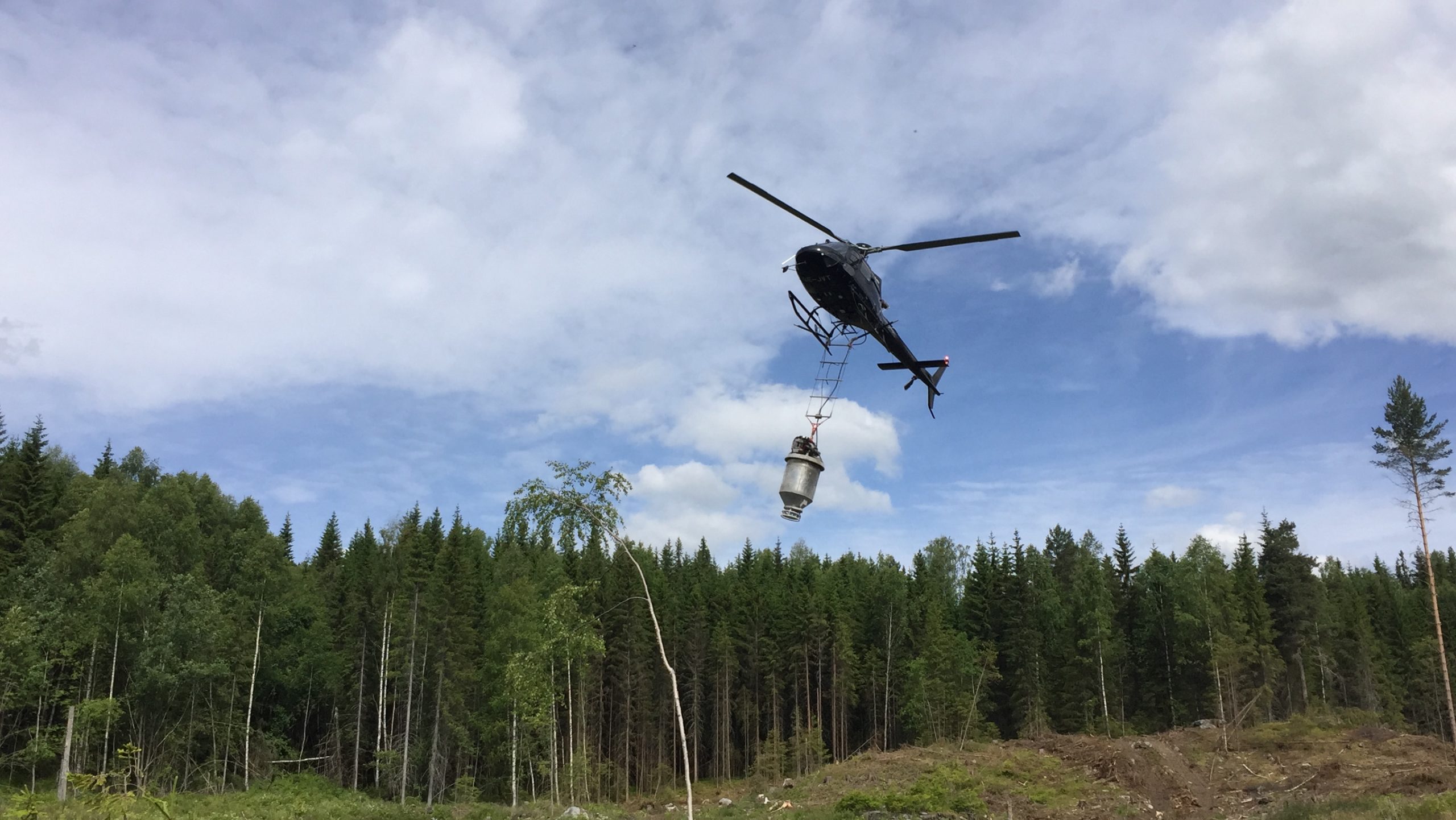 Helikopter flyr over skog og gjødsler.