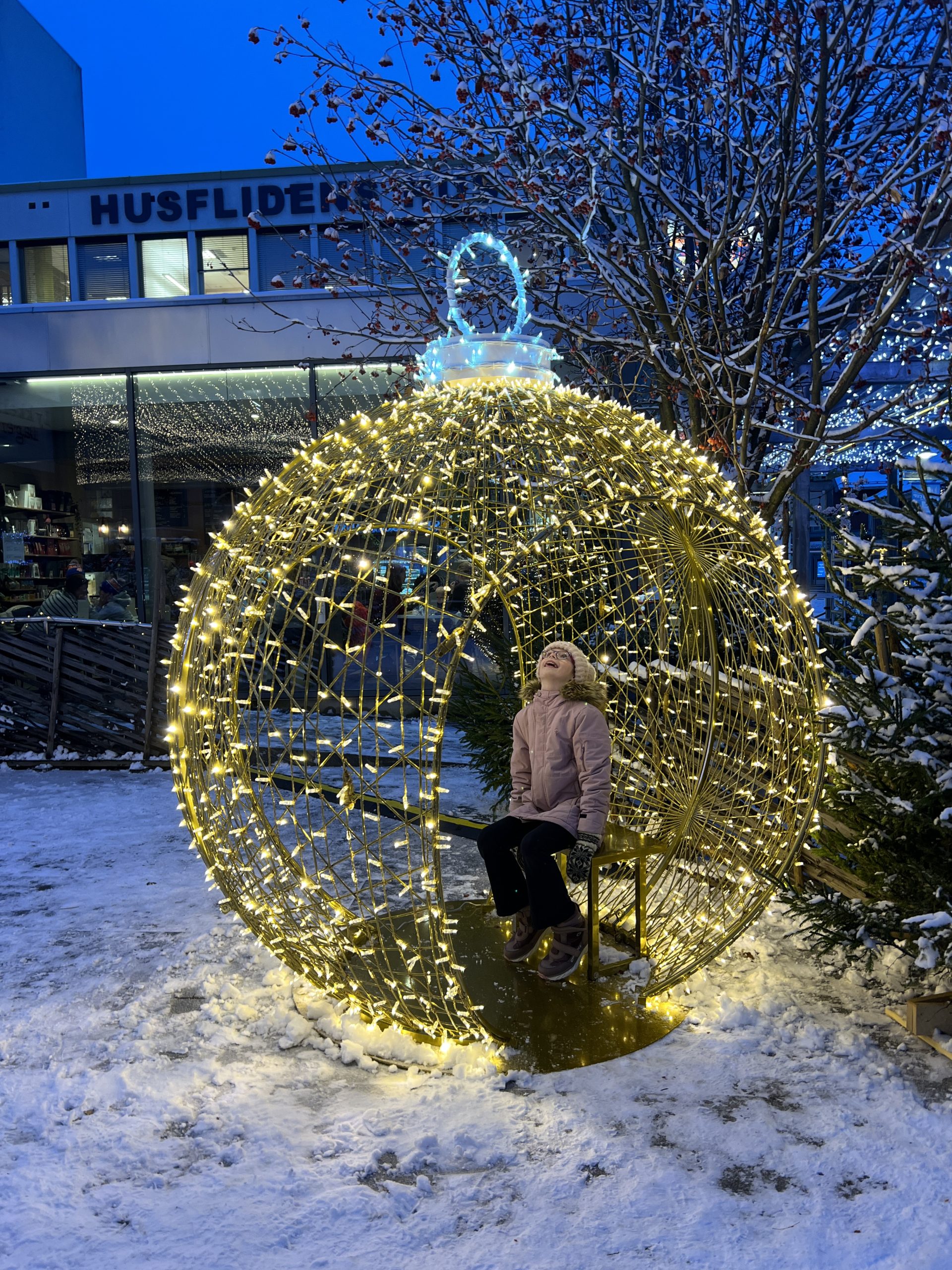 Jente sitter inni en lysinstallasjon formet som en stor julekule.