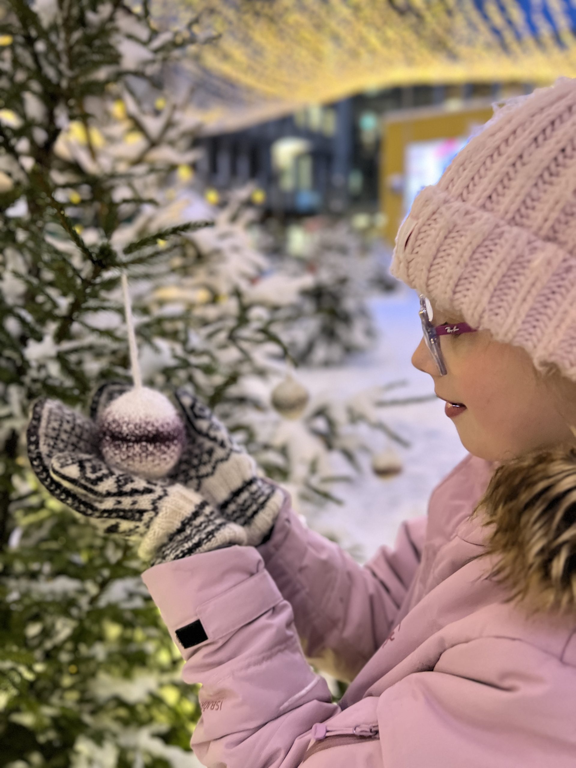 Jente holder under en strikket julekule som henger i et juletre.